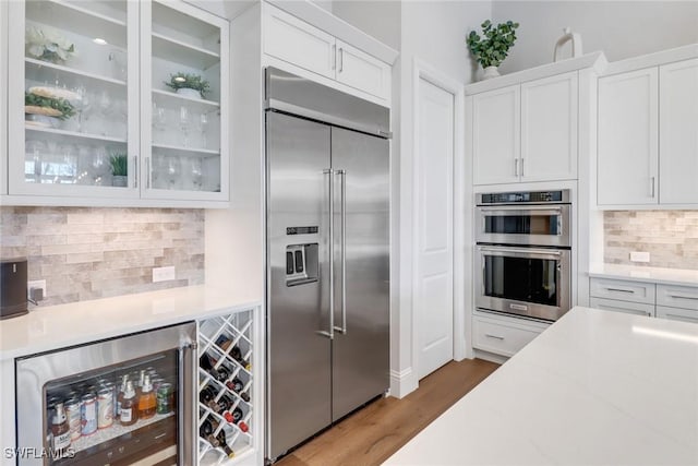 kitchen with wine cooler, stainless steel appliances, white cabinets, tasteful backsplash, and glass insert cabinets