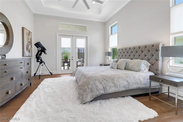 bedroom with access to exterior, french doors, a raised ceiling, and dark wood finished floors