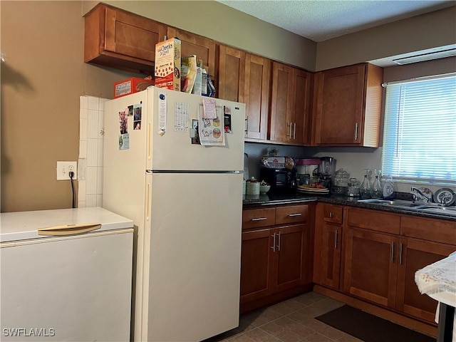 kitchen with dark stone counters, sink, white fridge, and a textured ceiling