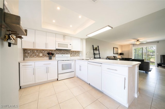 kitchen featuring white appliances, white cabinets, ceiling fan, a tray ceiling, and kitchen peninsula