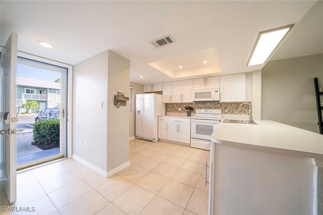 kitchen with sink, a raised ceiling, kitchen peninsula, white appliances, and white cabinets