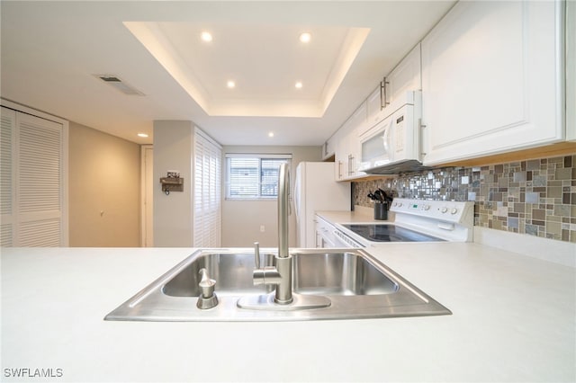 kitchen with sink, a raised ceiling, backsplash, white appliances, and white cabinets