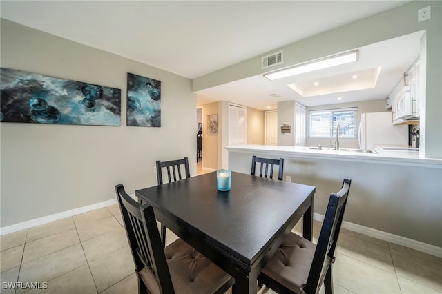 dining area with a raised ceiling, light tile patterned floors, and sink