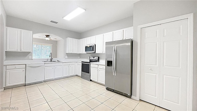 kitchen with appliances with stainless steel finishes, ceiling fan, sink, white cabinets, and light tile patterned flooring