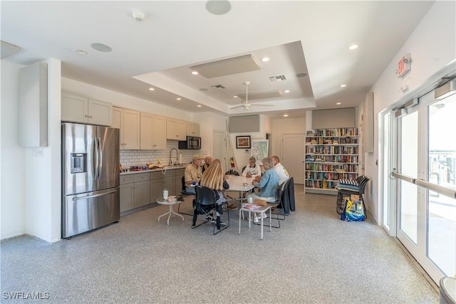 kitchen with gray cabinetry, sink, stainless steel refrigerator with ice dispenser, decorative backsplash, and a tray ceiling