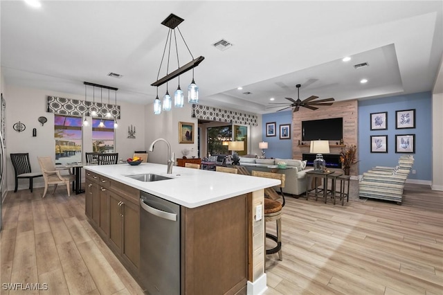 kitchen featuring dishwasher, a raised ceiling, sink, and an island with sink