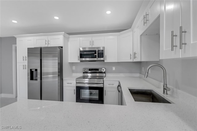 kitchen featuring white cabinets, light stone countertops, stainless steel appliances, and a sink