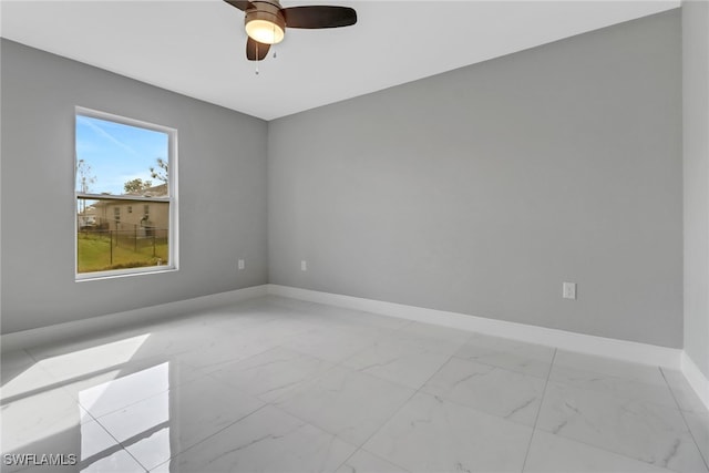 spare room with a ceiling fan, marble finish floor, and baseboards