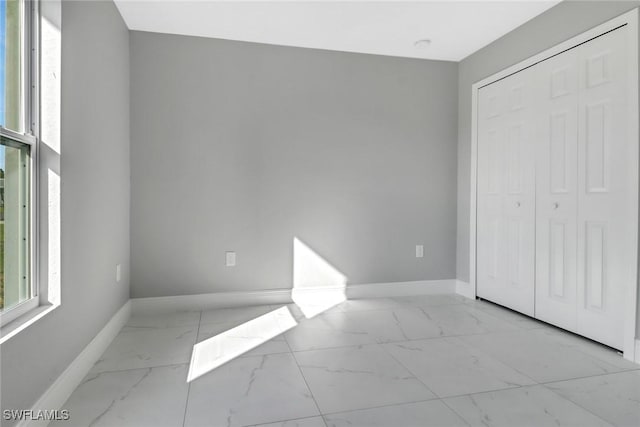 unfurnished bedroom featuring a closet, marble finish floor, and baseboards