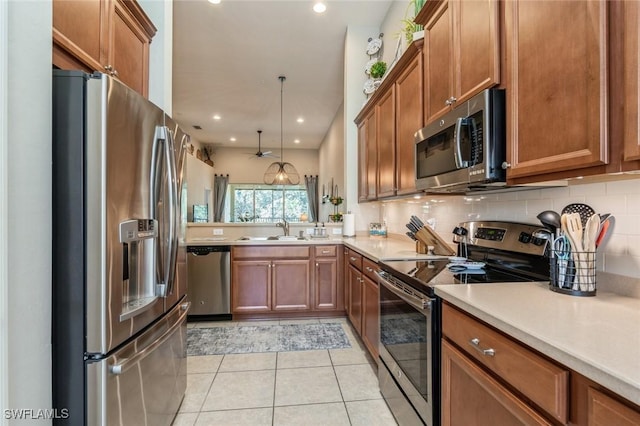 kitchen featuring light tile patterned floors, kitchen peninsula, appliances with stainless steel finishes, hanging light fixtures, and sink