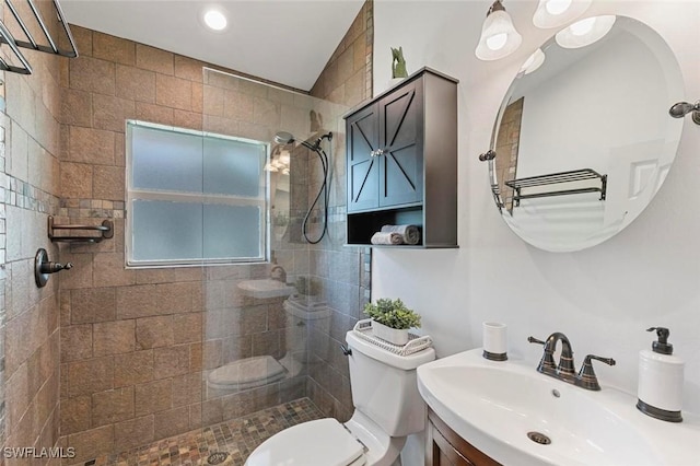 bathroom with a tile shower, vanity, toilet, and lofted ceiling