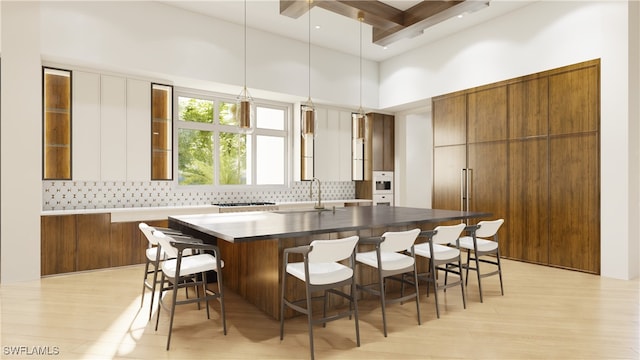 kitchen featuring pendant lighting, an island with sink, sink, backsplash, and light wood-type flooring