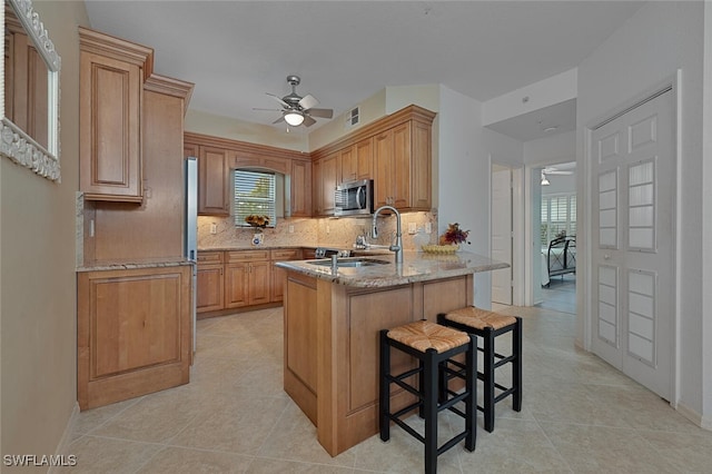 kitchen with a kitchen bar, kitchen peninsula, tasteful backsplash, light stone countertops, and sink