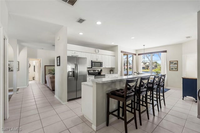 kitchen with appliances with stainless steel finishes, light tile patterned flooring, a breakfast bar, and white cabinetry