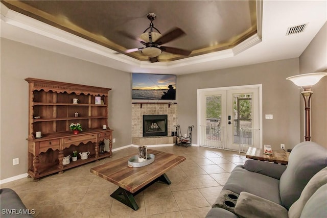 tiled living room featuring ceiling fan, french doors, a fireplace, and a tray ceiling