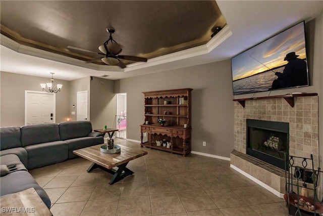 tiled living room with a tray ceiling, a tiled fireplace, and ceiling fan with notable chandelier