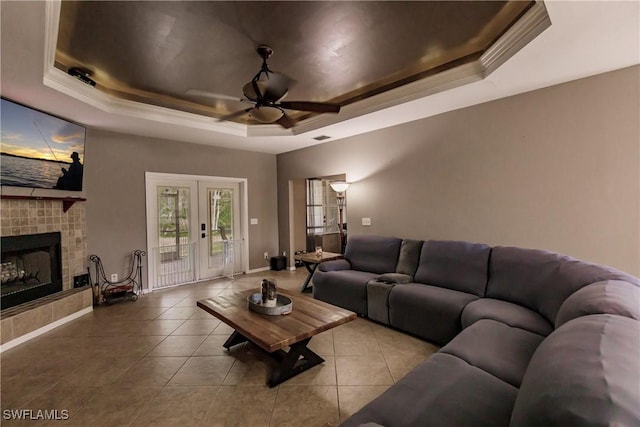 living room featuring ceiling fan, a raised ceiling, a tile fireplace, and french doors