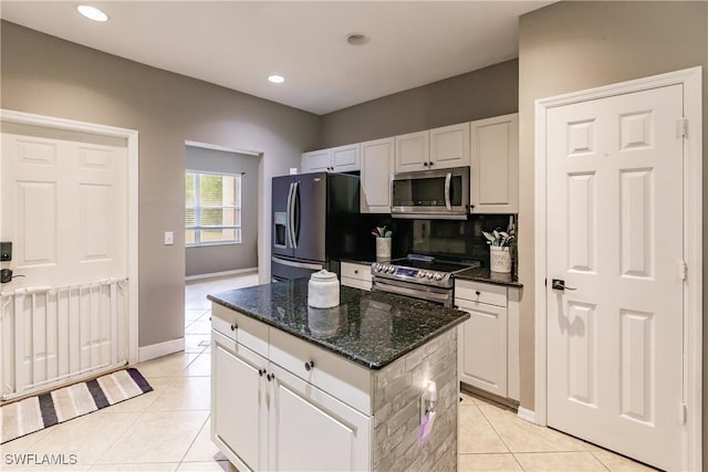 kitchen with stainless steel appliances, a kitchen island, white cabinets, dark stone countertops, and light tile patterned flooring