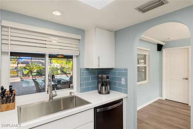 kitchen featuring backsplash, dishwasher, white cabinets, and light hardwood / wood-style flooring