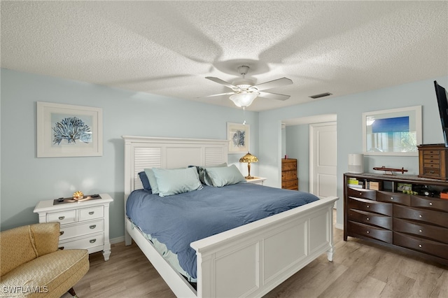 bedroom with ceiling fan, light wood-type flooring, and a textured ceiling