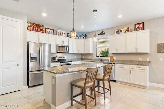 kitchen with appliances with stainless steel finishes, light tile patterned floors, stone countertops, white cabinets, and a center island