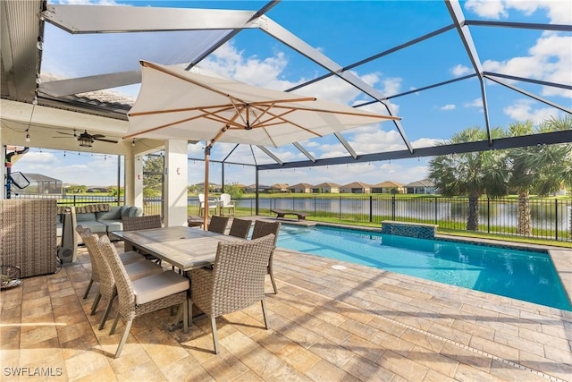 view of swimming pool with glass enclosure, a patio area, a water view, and ceiling fan