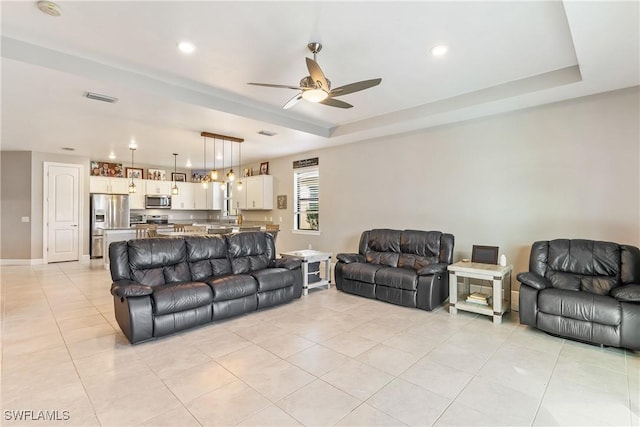 tiled living room with a tray ceiling and ceiling fan