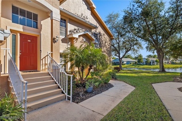 view of exterior entry with a water view and a yard