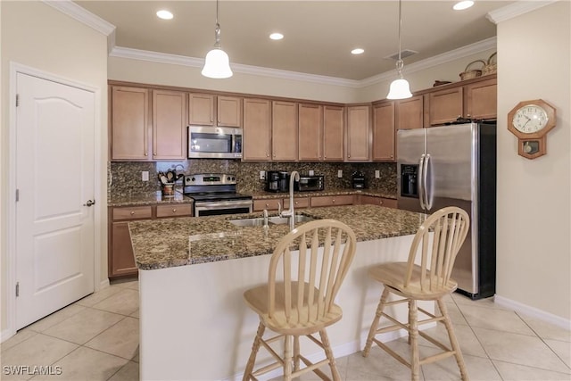 kitchen with pendant lighting, a center island with sink, light tile patterned floors, appliances with stainless steel finishes, and a breakfast bar area