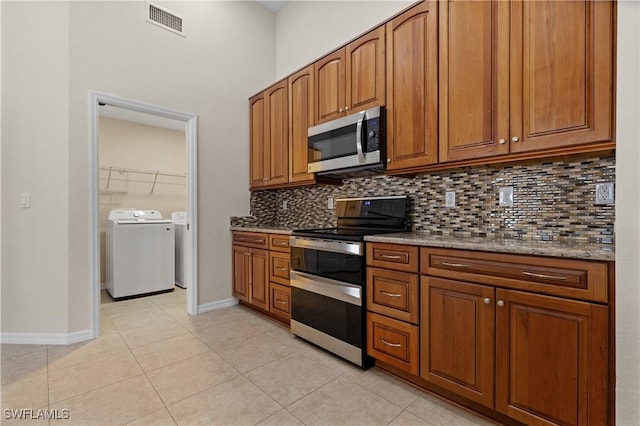 kitchen featuring decorative backsplash, appliances with stainless steel finishes, light stone countertops, washer and clothes dryer, and light tile patterned floors