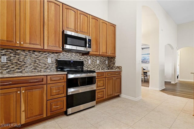 kitchen with decorative backsplash, light tile patterned flooring, a high ceiling, and appliances with stainless steel finishes