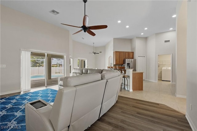 living room with washer / dryer, light tile patterned floors, ceiling fan, and a high ceiling