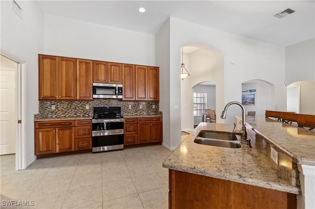 kitchen featuring light stone countertops, tasteful backsplash, stainless steel appliances, sink, and a high ceiling