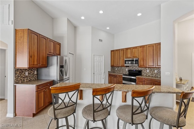 kitchen with light tile patterned floors, a high ceiling, a kitchen breakfast bar, a kitchen island, and appliances with stainless steel finishes