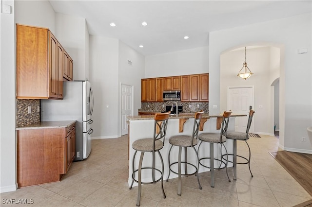 kitchen featuring light stone countertops, hanging light fixtures, a high ceiling, an island with sink, and appliances with stainless steel finishes