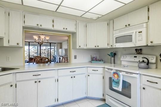 kitchen with a notable chandelier, white appliances, white cabinets, and light tile patterned floors