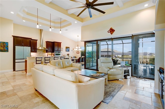 living room with crown molding, a high ceiling, ceiling fan with notable chandelier, and a raised ceiling