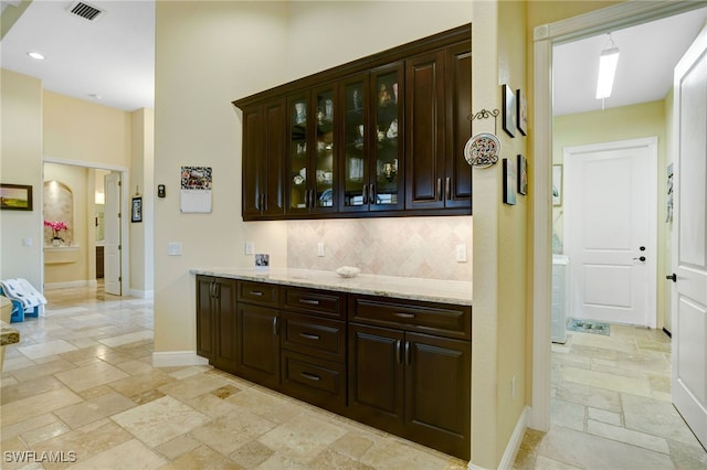 bar featuring light stone counters, tasteful backsplash, and dark brown cabinetry