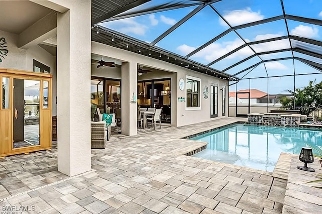 view of swimming pool featuring ceiling fan, a patio, glass enclosure, and an in ground hot tub