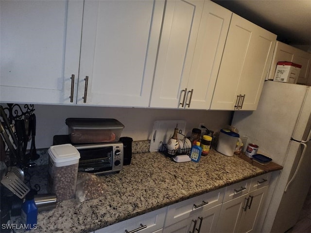 kitchen with white cabinets, stainless steel fridge, and light stone counters