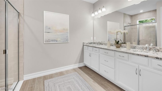 full bathroom featuring double vanity, wood finish floors, a stall shower, and baseboards