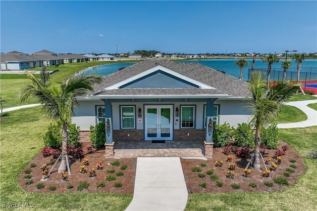 view of front of home with a shingled roof, a water view, french doors, a front lawn, and stucco siding