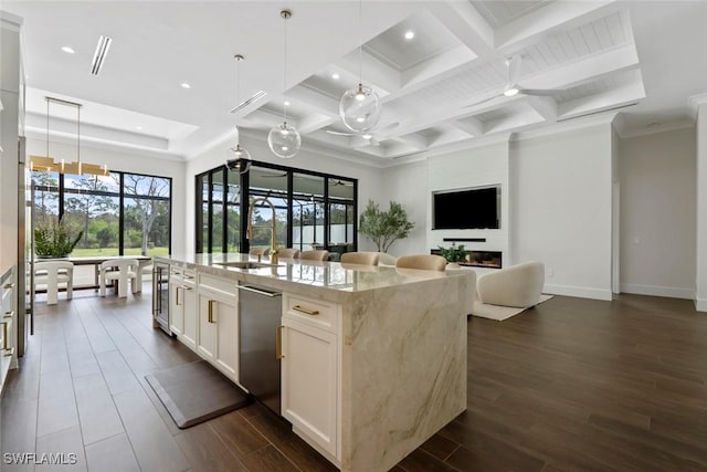 kitchen with a kitchen island with sink, hanging light fixtures, light stone countertops, and white cabinets