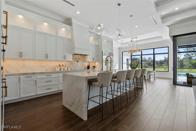 kitchen featuring a center island with sink, white cabinets, pendant lighting, light stone countertops, and backsplash