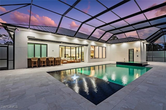 pool at dusk with a patio, a lanai, an outdoor living space, and an outdoor bar