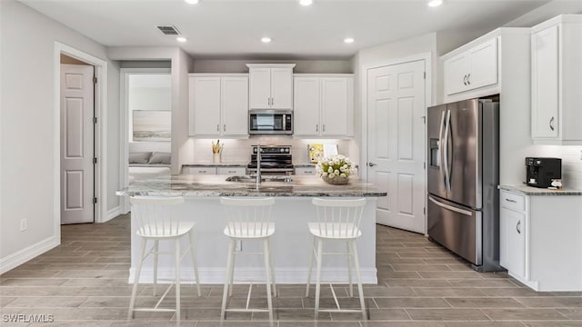 kitchen featuring white cabinets, appliances with stainless steel finishes, light stone countertops, and an island with sink