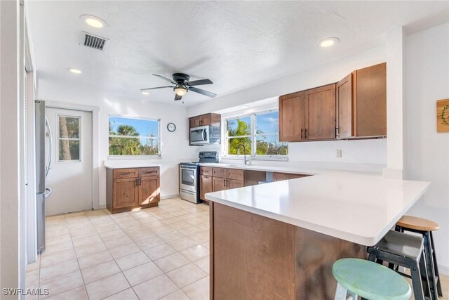 kitchen featuring kitchen peninsula, stainless steel appliances, ceiling fan, sink, and a breakfast bar area