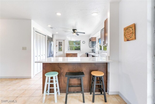 kitchen featuring ceiling fan, kitchen peninsula, a kitchen bar, light tile patterned floors, and appliances with stainless steel finishes