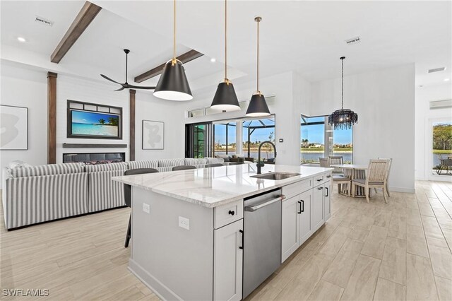 kitchen with a center island with sink, white cabinets, sink, stainless steel dishwasher, and light stone countertops