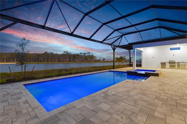 pool at dusk with glass enclosure, exterior kitchen, an in ground hot tub, a water view, and a patio